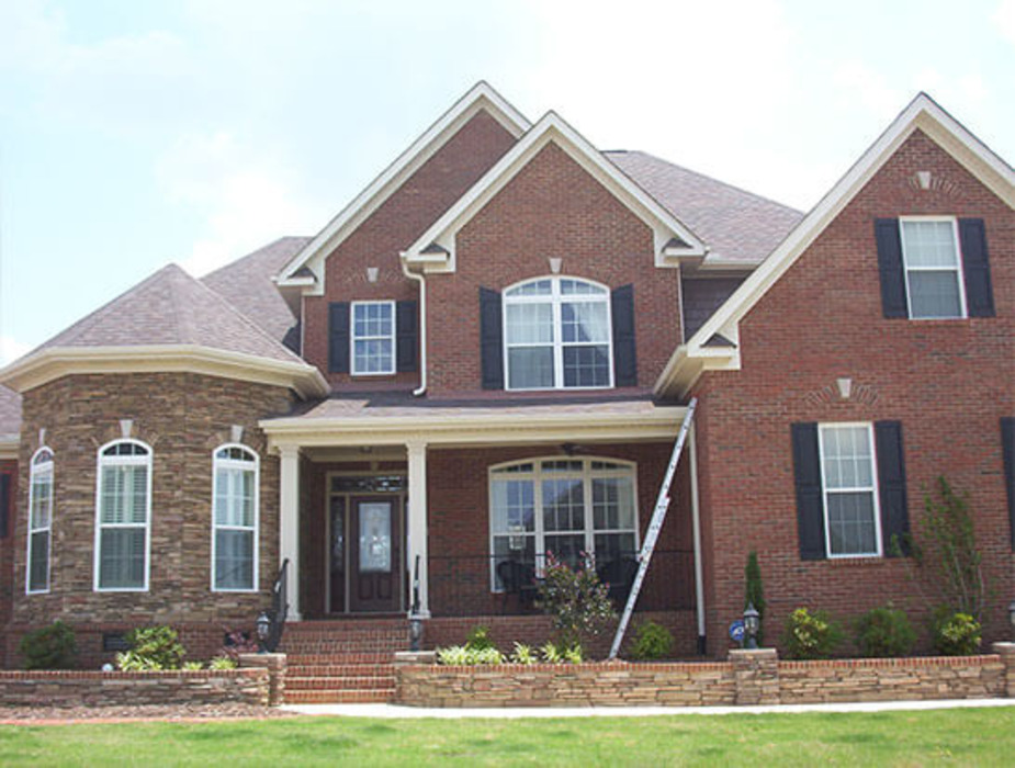Brick residential home with a multi-gabled shingle roof, white trim, and multiple windows, showcasing residential roofing construction.
